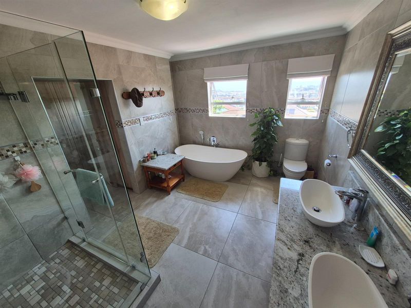 Modern bathroom featuring a freestanding bathtub, glass-enclosed shower, dual vanity with granite countertop, and neutral floor-to-ceiling tiling.