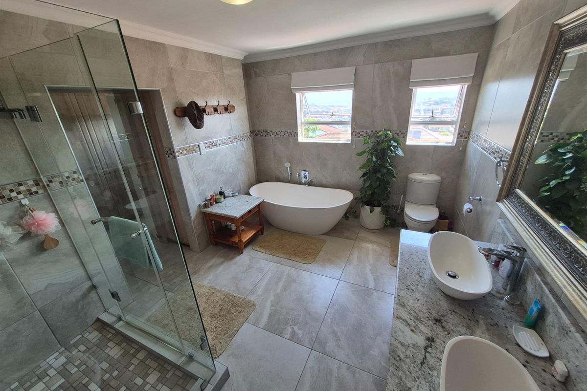 Modern bathroom featuring a freestanding bathtub, glass-enclosed shower, dual vanity with granite countertop, and neutral floor-to-ceiling tiling.