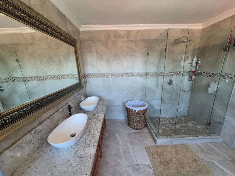 Modern bathroom featuring a double vanity with granite countertop, vessel sinks, and a spacious glass-enclosed walk-in shower with tiled walls.