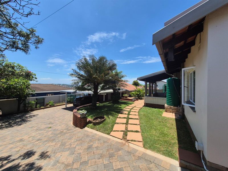 A well-maintained exterior view featuring a paved driveway, landscaped garden with a stone pathway, and a covered patio area with a water tank.