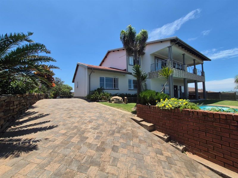 A two-story residential property featuring a paved driveway, a covered balcony, and a swimming pool area with brick retaining walls.
