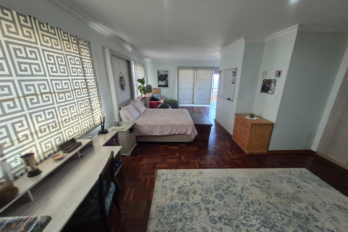 Spacious bedroom featuring polished parquet flooring, recessed ceiling lighting, and large windows with patterned privacy screens.