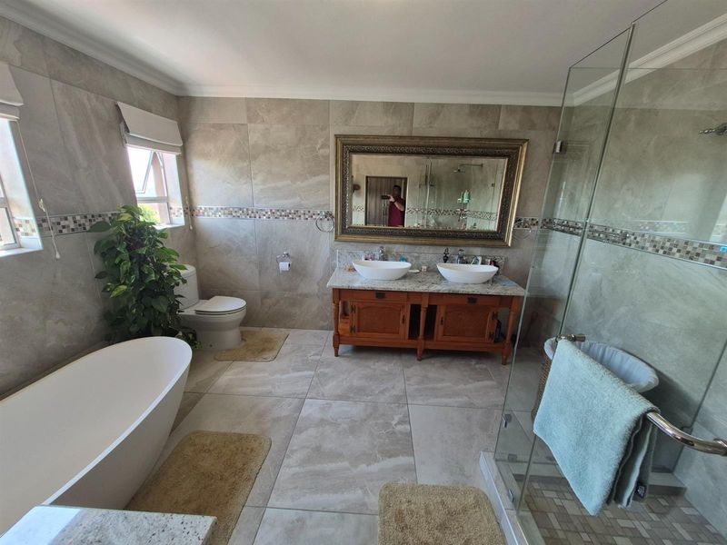 Modern bathroom featuring a double vanity with granite countertop, freestanding bathtub, and a glass-enclosed walk-in shower with neutral floor-to-ceiling tiling.