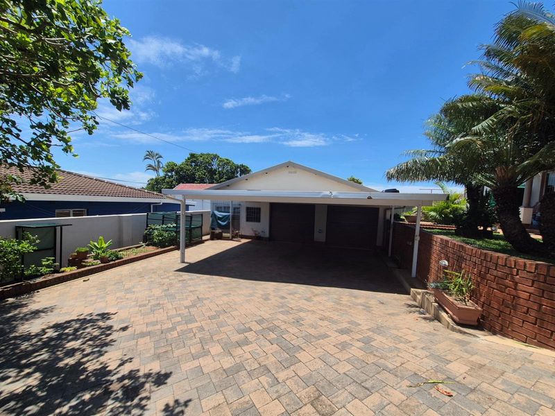 A paved driveway leading to a double garage with a covered carport structure, set within a landscaped residential property.