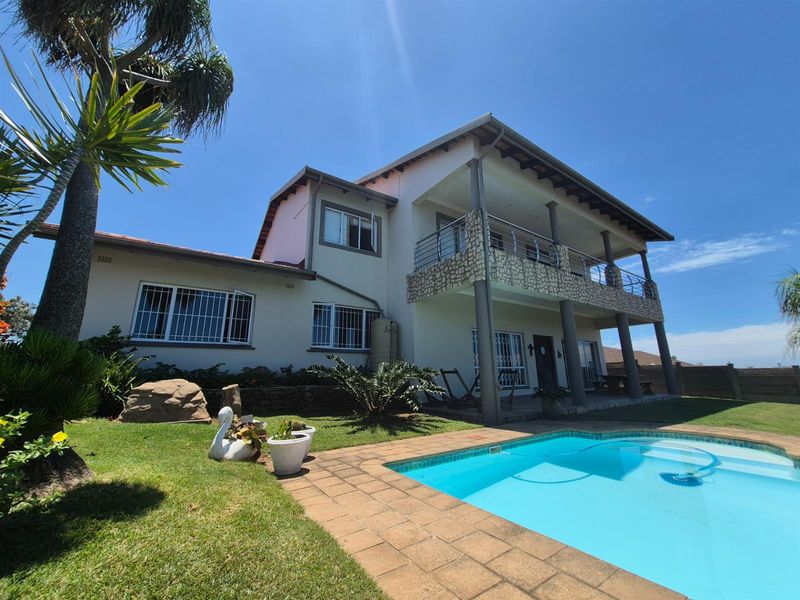 Rear view of a two-story house featuring a swimming pool, paved patio area, and a covered upper-level balcony with stone cladding.