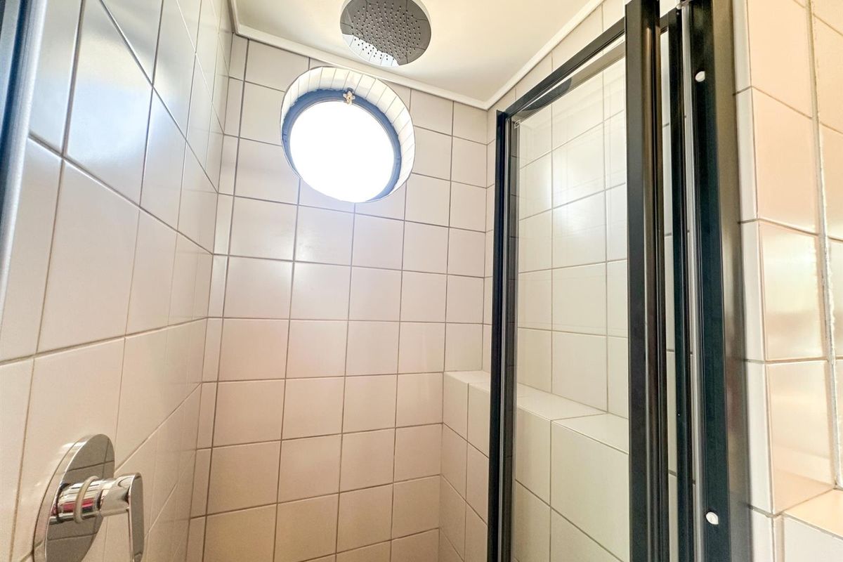A modern shower enclosure featuring white wall tiles, a circular porthole window, and a contemporary rainfall shower head with black frame detailing.