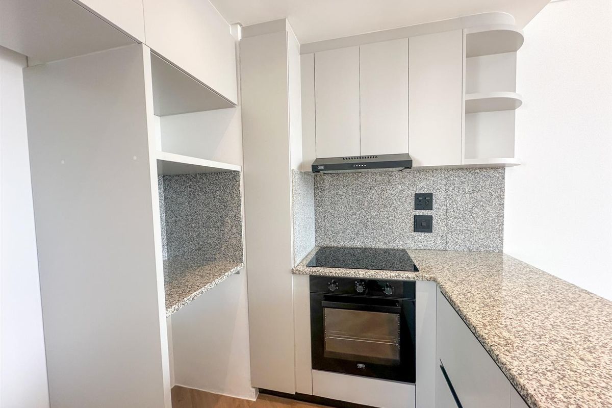 Modern kitchen featuring granite countertops, built-in oven, electric hob, extractor fan, and ample white cabinetry with open shelving.