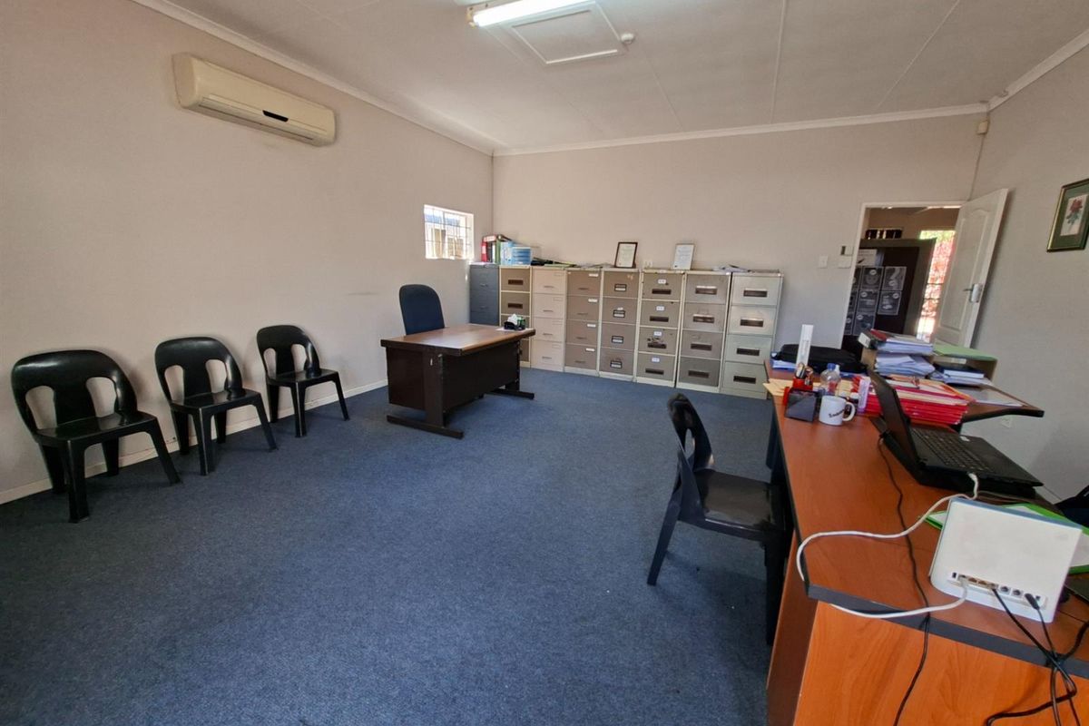A functional office space featuring carpeted flooring, wall-mounted air conditioning unit, and built-in storage cabinets.