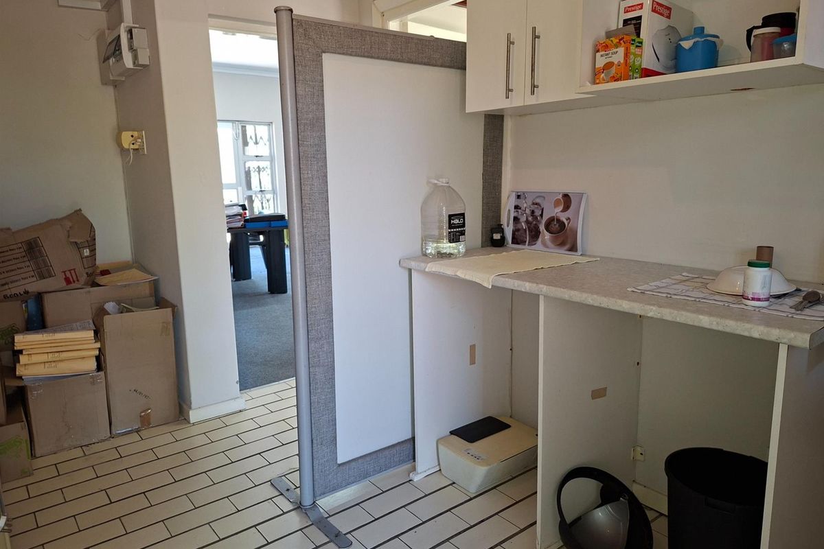 A functional office kitchenette area featuring built-in cabinetry, tiled flooring, and a partition screen, providing a practical space for staff refreshments.