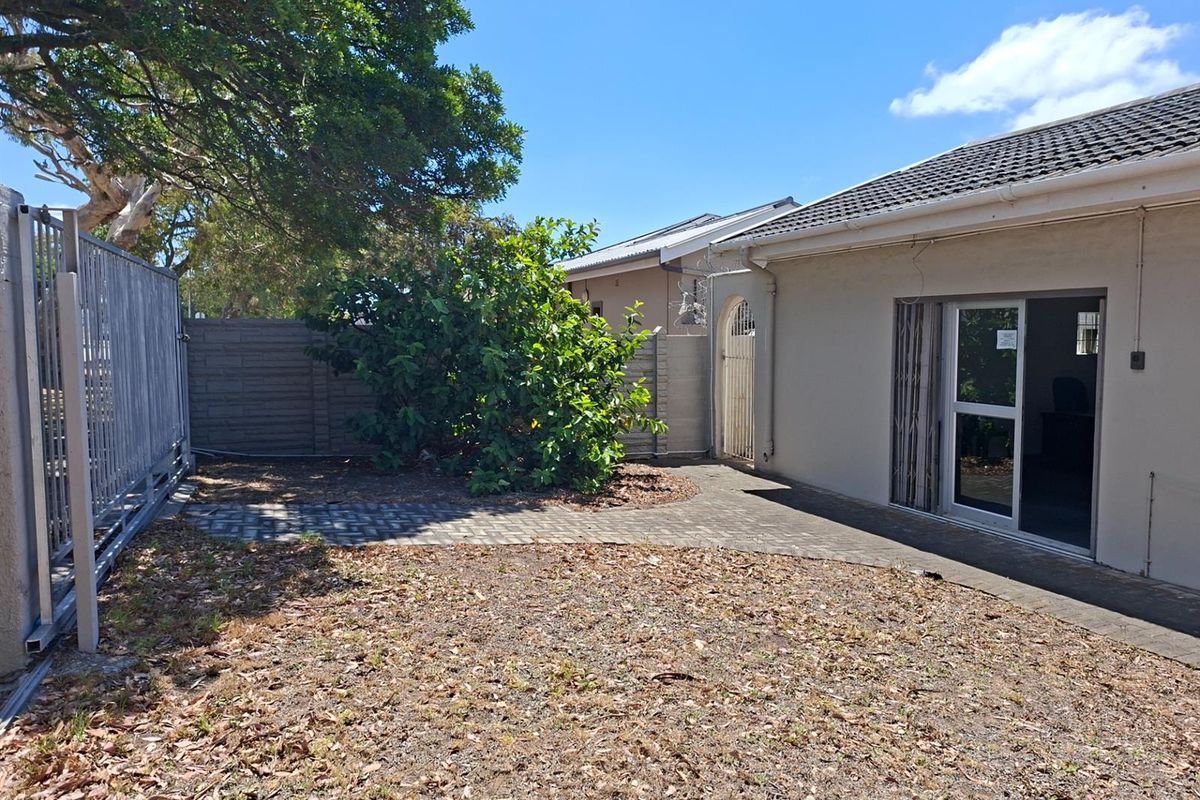 Rear exterior view of the office property featuring a paved patio area, perimeter walling, and established garden space.