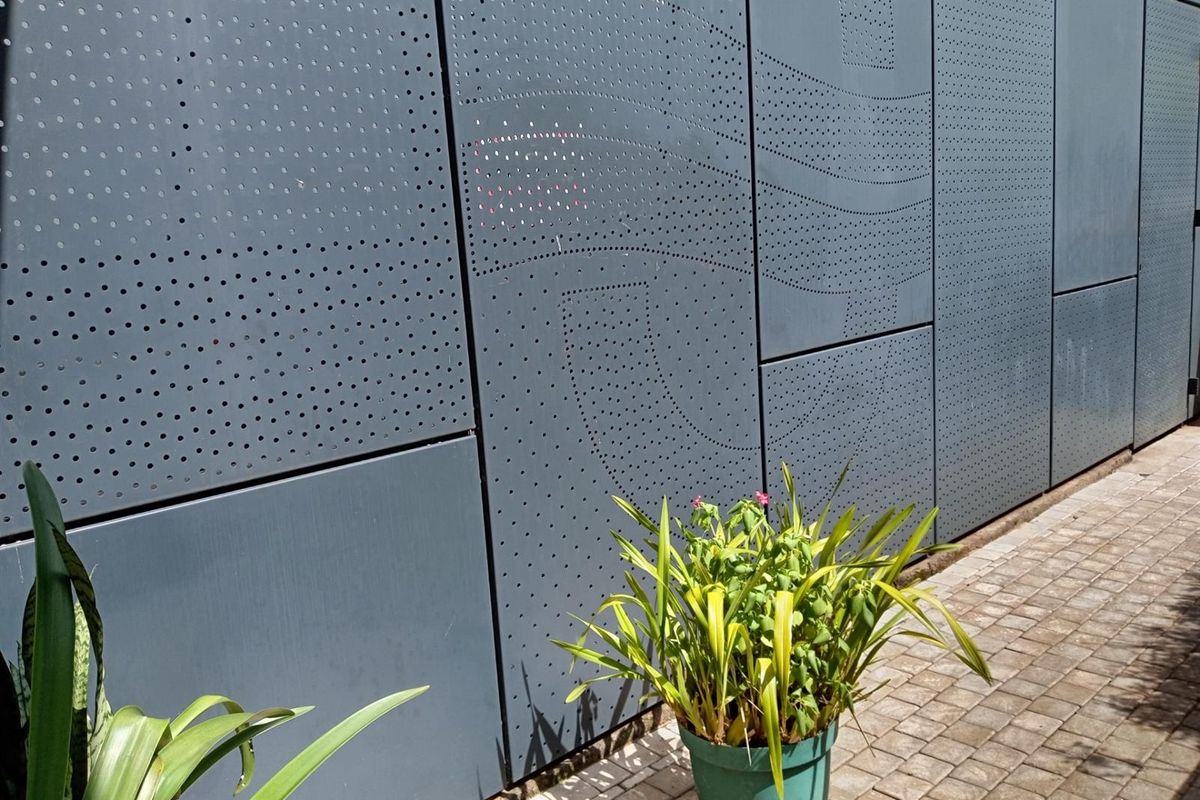 A modern exterior wall featuring decorative perforated metal cladding panels, complemented by a paved walkway.