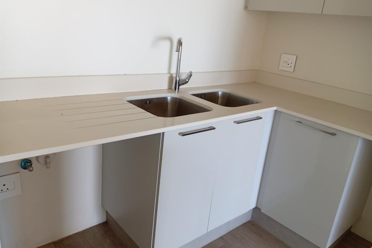 A clean, modern kitchen area featuring a double stainless steel sink, integrated cabinetry, and plumbing connections for an appliance.