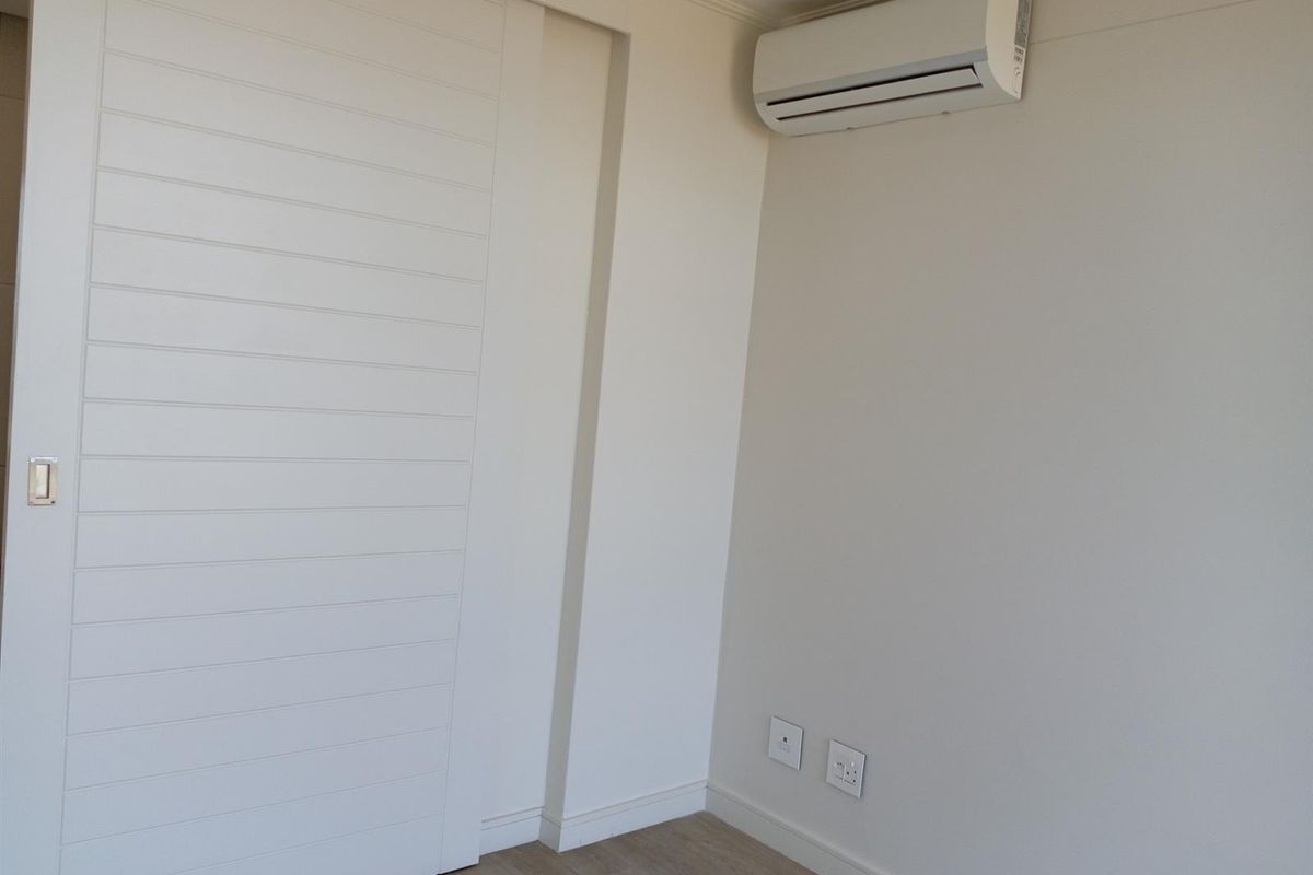 A clean, neutral bedroom interior featuring a wall-mounted air conditioning unit, modern sliding door, and light wood-look flooring.