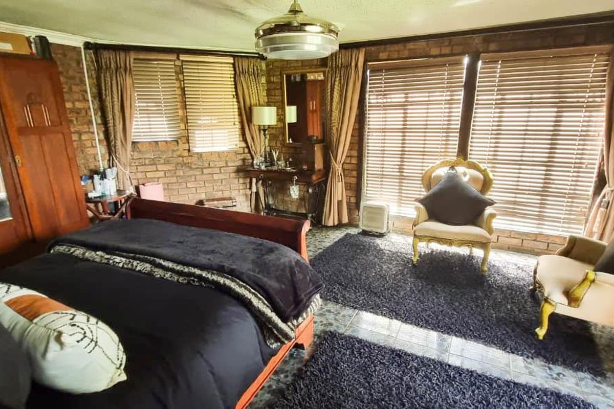 Spacious bedroom featuring exposed brick walls, tiled flooring, and large windows with venetian blinds, offering a rustic and character-filled living space.