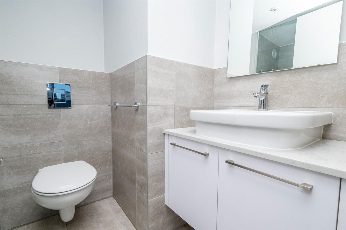Modern bathroom featuring a wall-mounted toilet, floating vanity with a countertop basin, and neutral grey wall tiling.