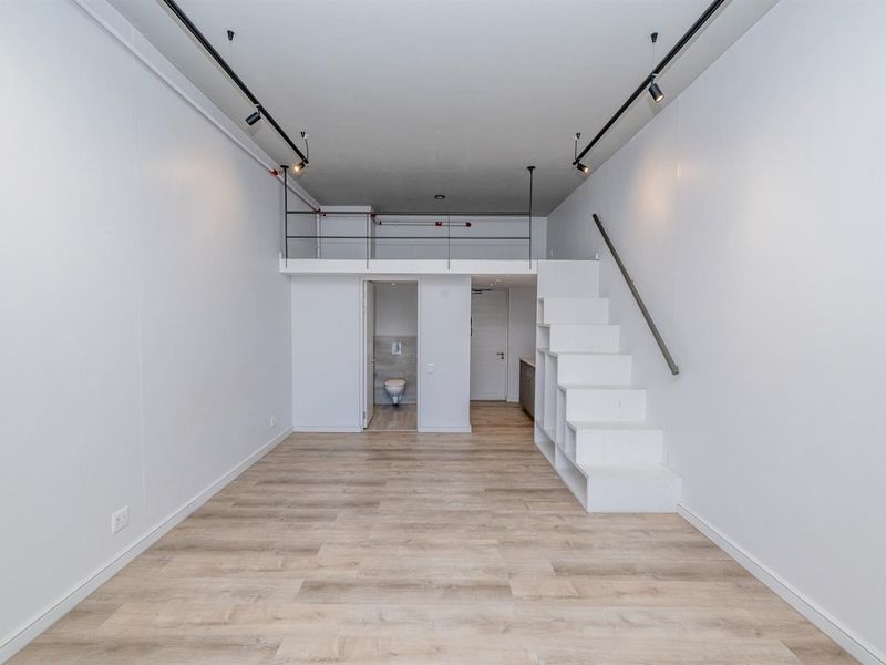 Modern open-plan apartment featuring a mezzanine level, built-in staircase with storage, track lighting, and light wood-look flooring.