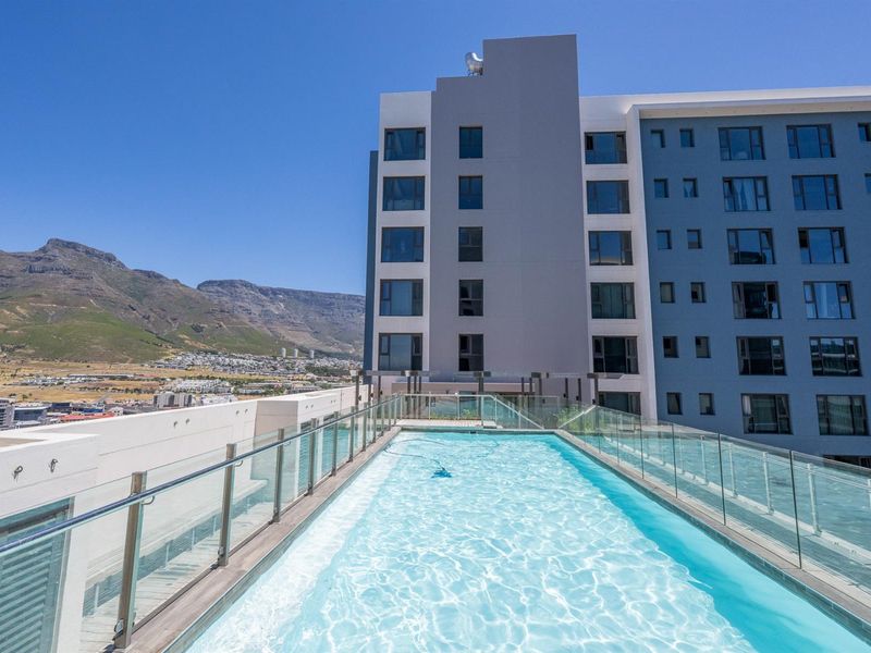 Rooftop swimming pool with glass balustrades, offering panoramic mountain and city views from the apartment complex.