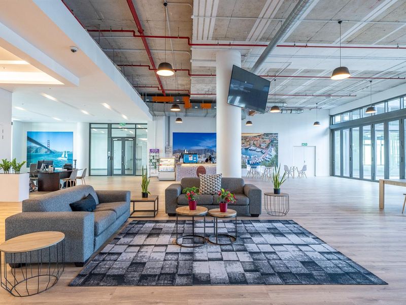 Spacious open-plan commercial or residential lobby area featuring industrial-style exposed concrete ceilings, modern flooring, and large glass panel doors leading to an outdoor space.