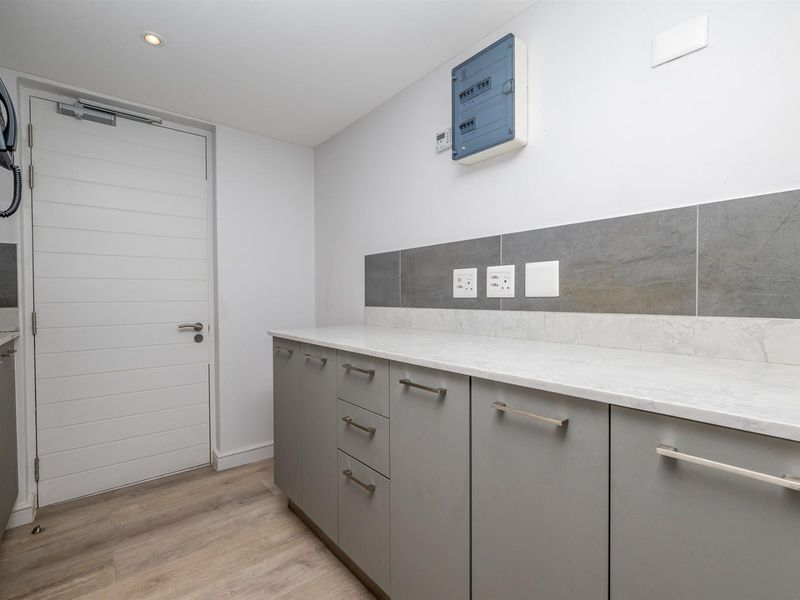 A functional laundry area featuring modern grey cabinetry, stone-look countertops, tiled splashback, and a secure internal door.
