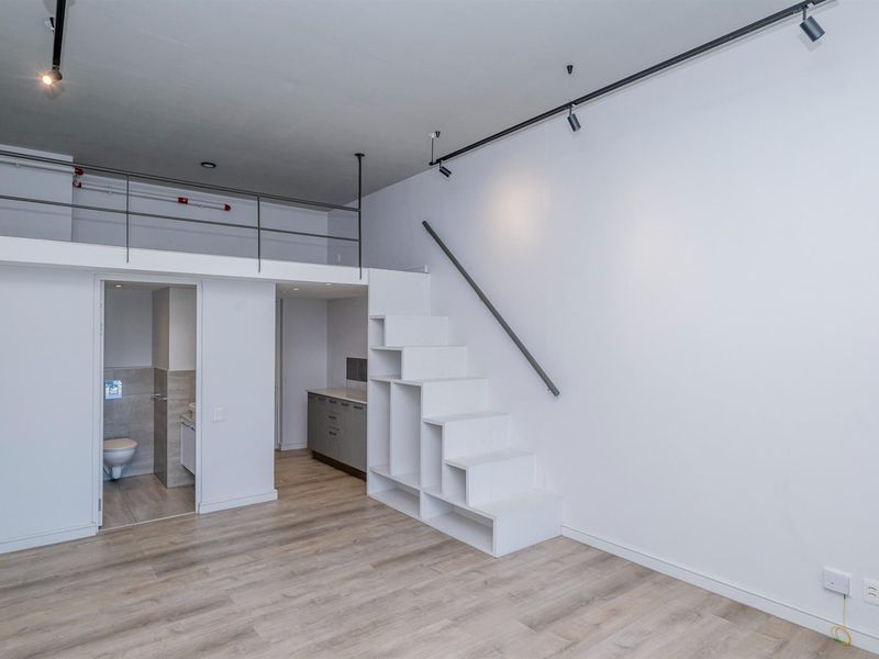 Modern open-plan apartment featuring a mezzanine level, built-in staircase storage, track lighting, and an integrated bathroom.