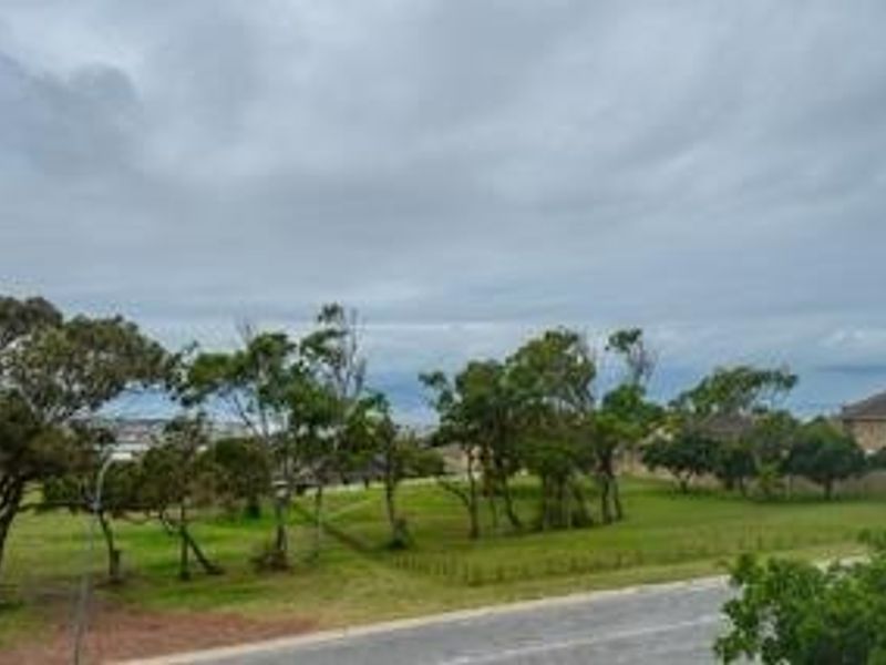 An elevated view overlooking a green park area with mature trees and a nearby road under a cloudy sky.