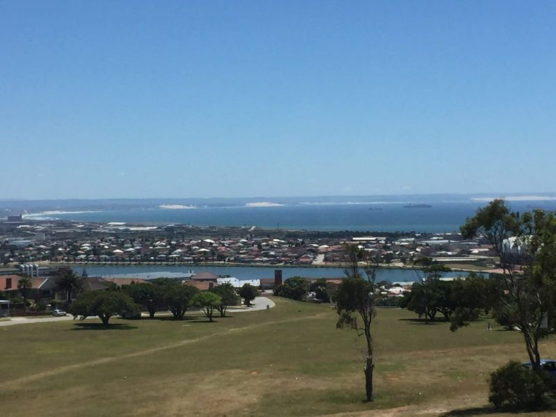 A wide-angle elevated view overlooking a coastal landscape, including a river, residential area, and the ocean in the distance.