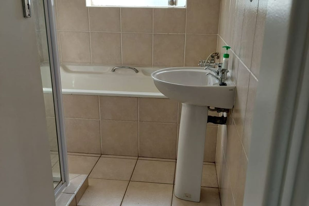 A functional bathroom featuring a pedestal basin, bathtub, and separate shower enclosure with neutral wall and floor tiling.