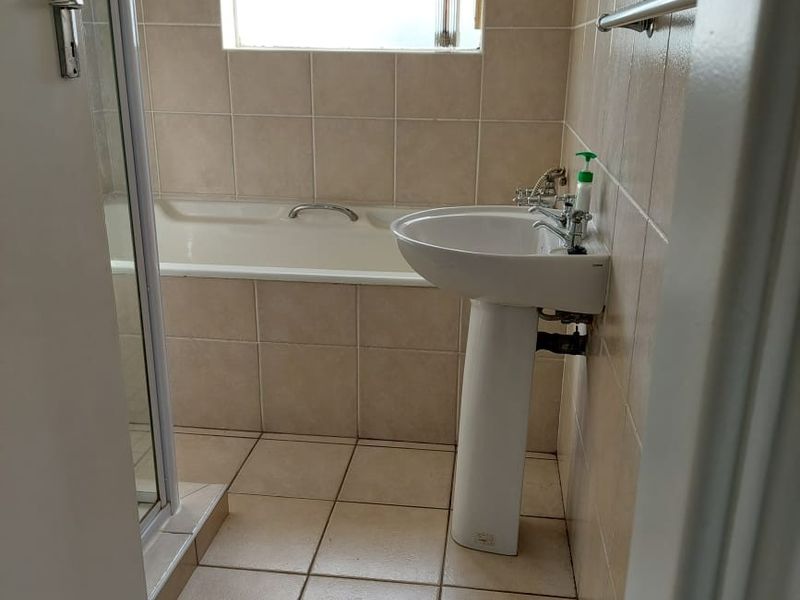 A functional bathroom featuring a pedestal basin, bathtub, and separate shower enclosure with neutral wall and floor tiling.