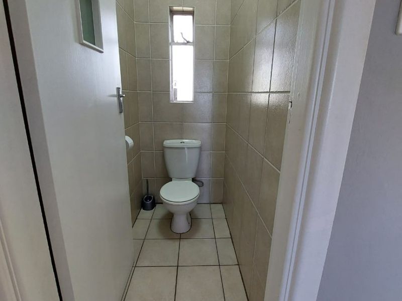 A compact, tiled guest bathroom featuring a standard toilet and a small window, providing a functional and clean space.