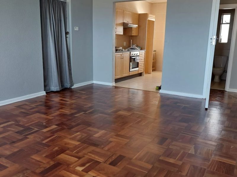 Spacious living area featuring polished parquet flooring and crown molding, with an open transition to a functional kitchen and adjacent bathroom access.