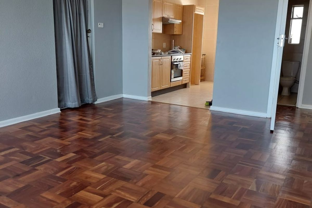 Spacious living area featuring polished parquet flooring and crown molding, with an open transition to a functional kitchen and adjacent bathroom access.