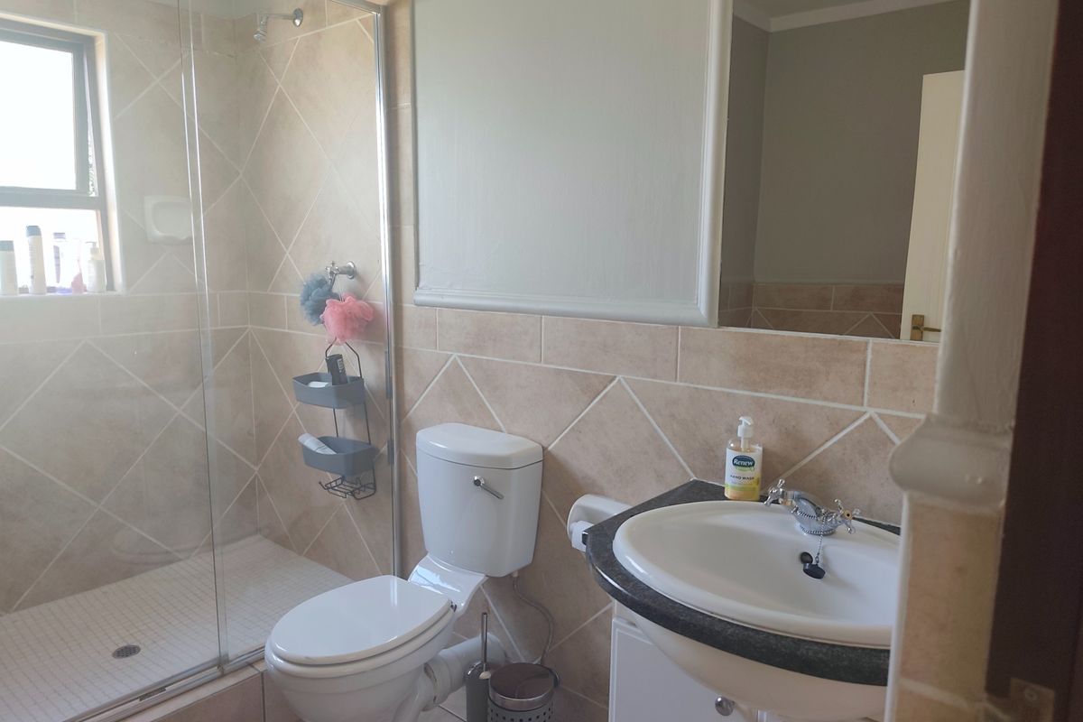 A functional bathroom featuring a glass-enclosed shower, vanity basin, and neutral ceramic tiling throughout.