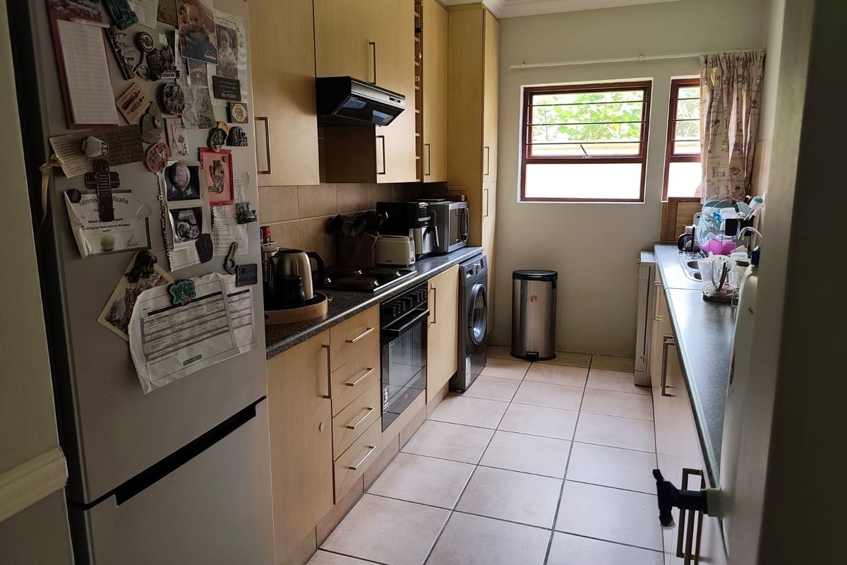 A functional galley-style kitchen featuring light wood cabinetry, tiled flooring, built-in oven, extractor fan, and a double sink with window views.