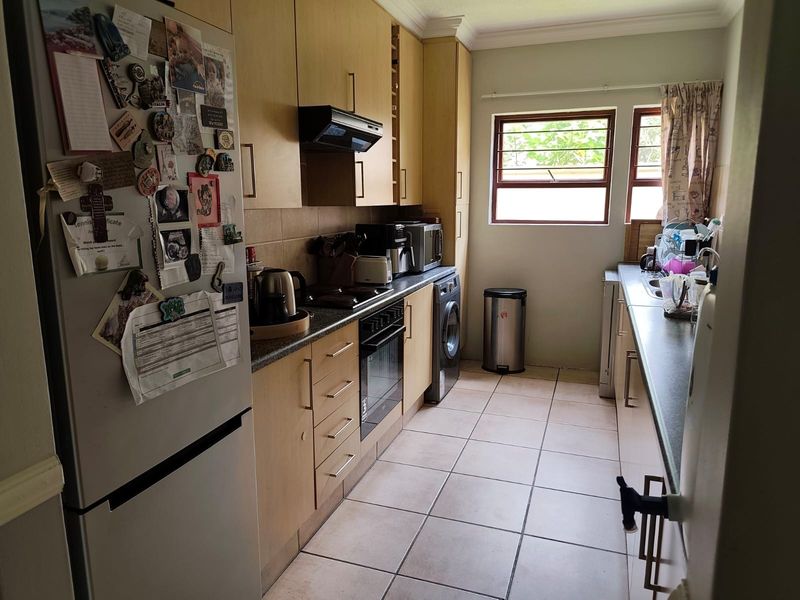 A functional galley-style kitchen featuring light wood cabinetry, tiled flooring, built-in oven, extractor fan, and a double sink with window views.
