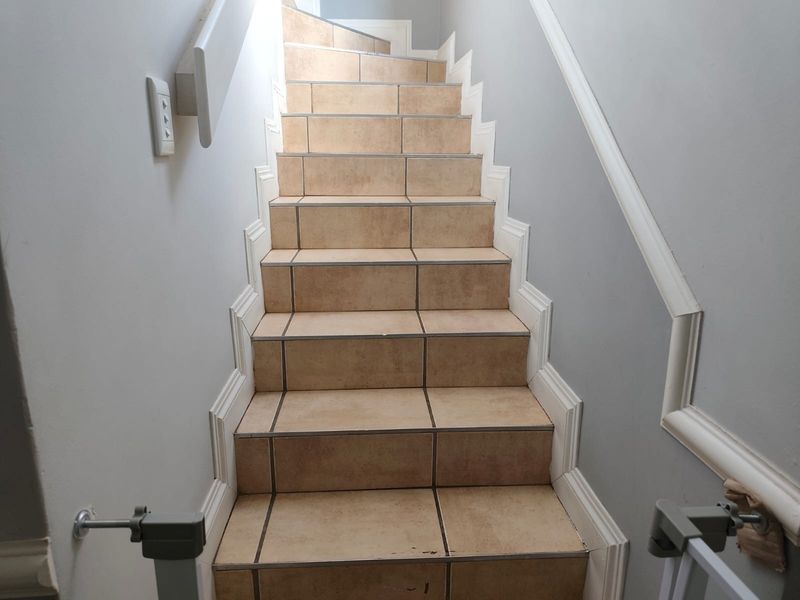 A staircase featuring tiled steps, decorative wall molding, and a handrail, providing access between levels in the home.
