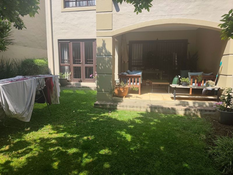 A rear view of the property featuring a covered patio area with tiled flooring, adjacent to a private garden and lawn.