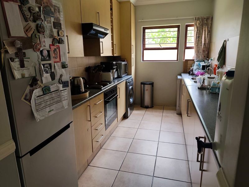 A functional galley-style kitchen featuring light wood-finish cabinetry, laminate countertops, built-in oven with extractor, and tiled flooring.