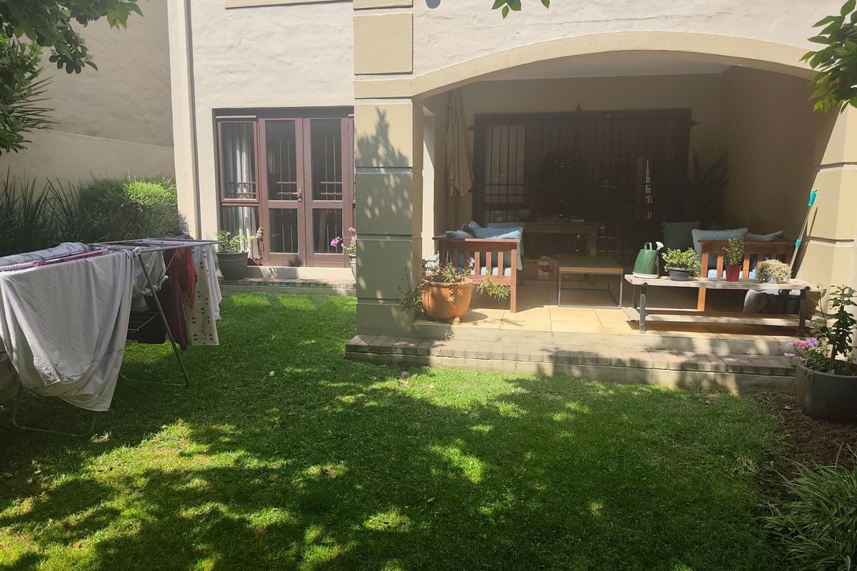A rear view of the property featuring a covered patio area with tiled flooring, adjacent to a private garden and lawn.