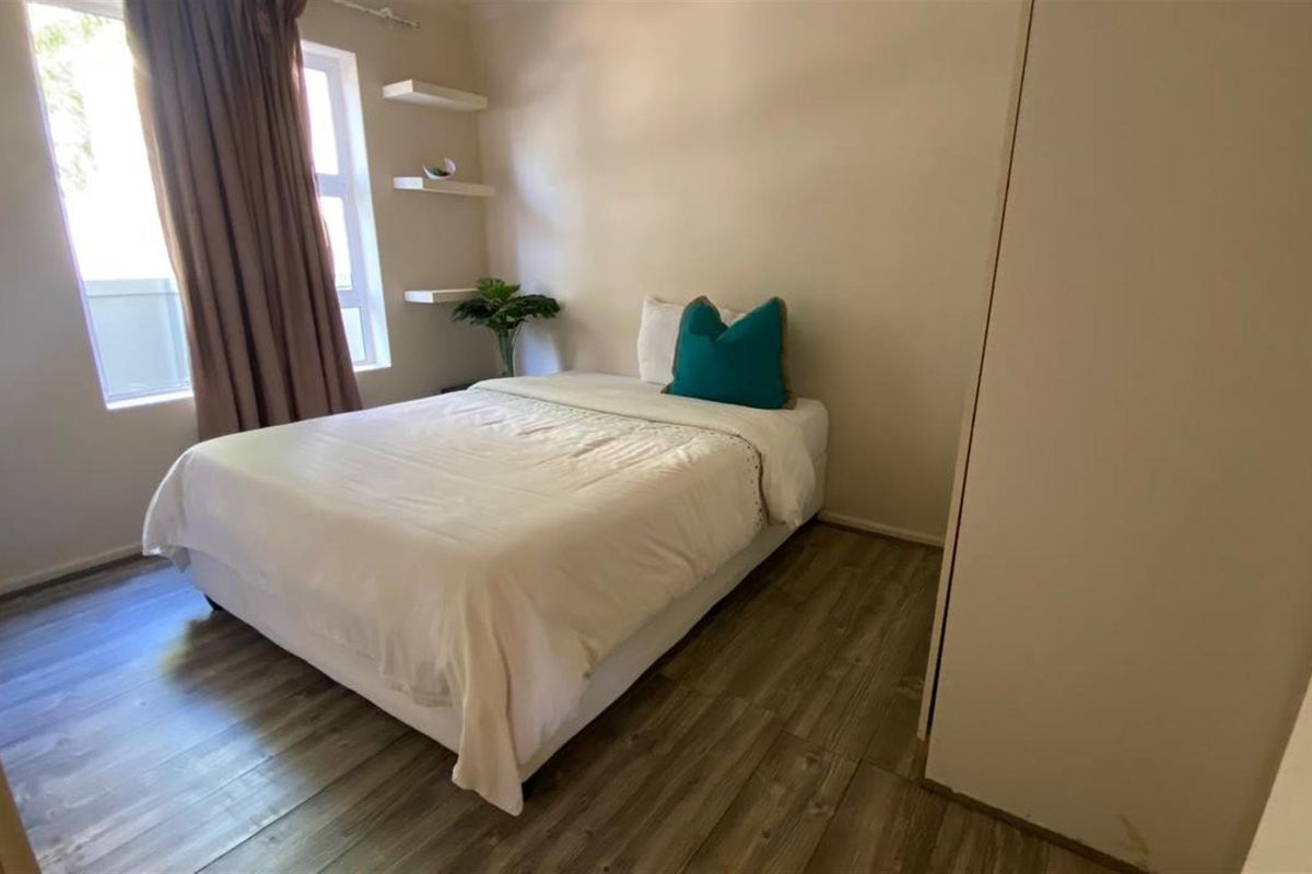 A well-lit bedroom featuring wood-look flooring, built-in shelving, and a large window with curtains.