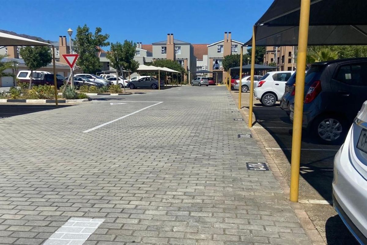 A paved outdoor parking area within the apartment complex, featuring designated parking bays with shade cloth structures.