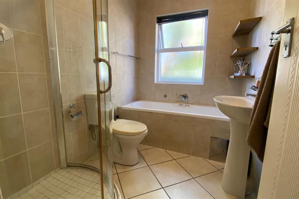 A functional bathroom featuring a glass-enclosed shower, a separate bathtub, a pedestal basin, and neutral wall and floor tiling.