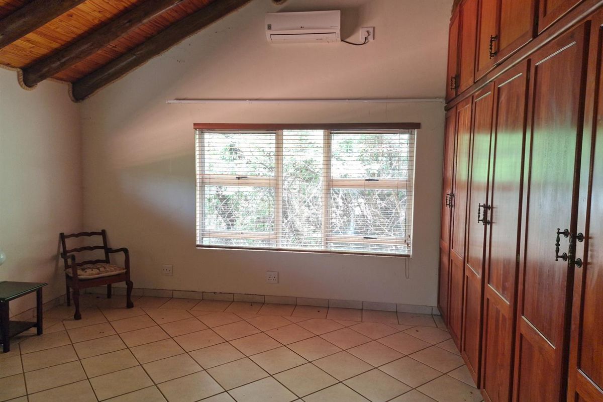A bedroom featuring a vaulted timber-beamed ceiling, tiled flooring, built-in wooden cabinetry, and a wall-mounted air conditioning unit.