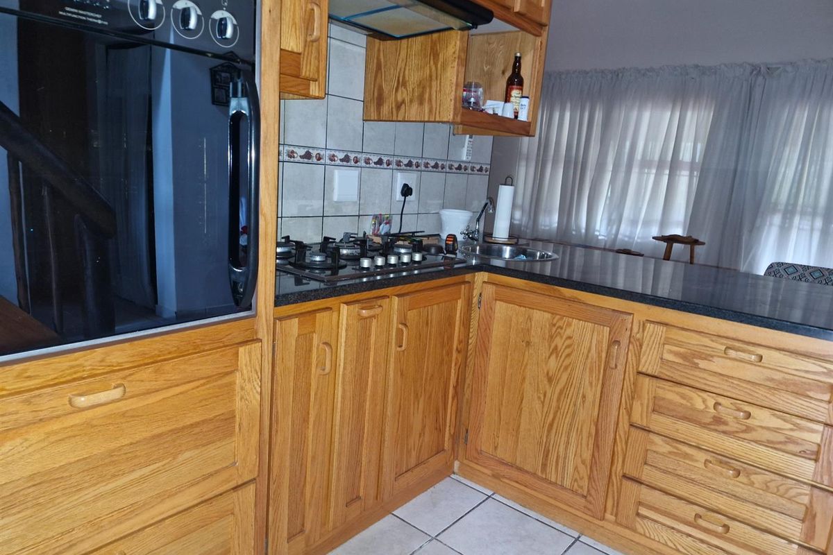 A functional kitchen featuring oak cabinetry, a built-in oven, gas hob, extractor fan, and dark granite countertops with tiled flooring.
