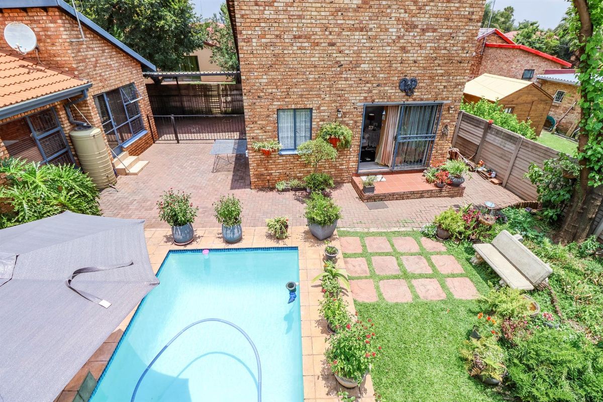 Aerial view of a private backyard featuring a swimming pool, paved patio area, established garden, and brick exterior facade.