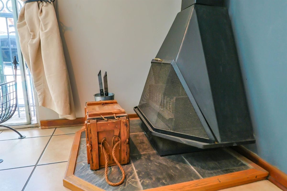 A corner-positioned black metal fireplace with a mesh screen, set on a tiled hearth with a wooden frame.
