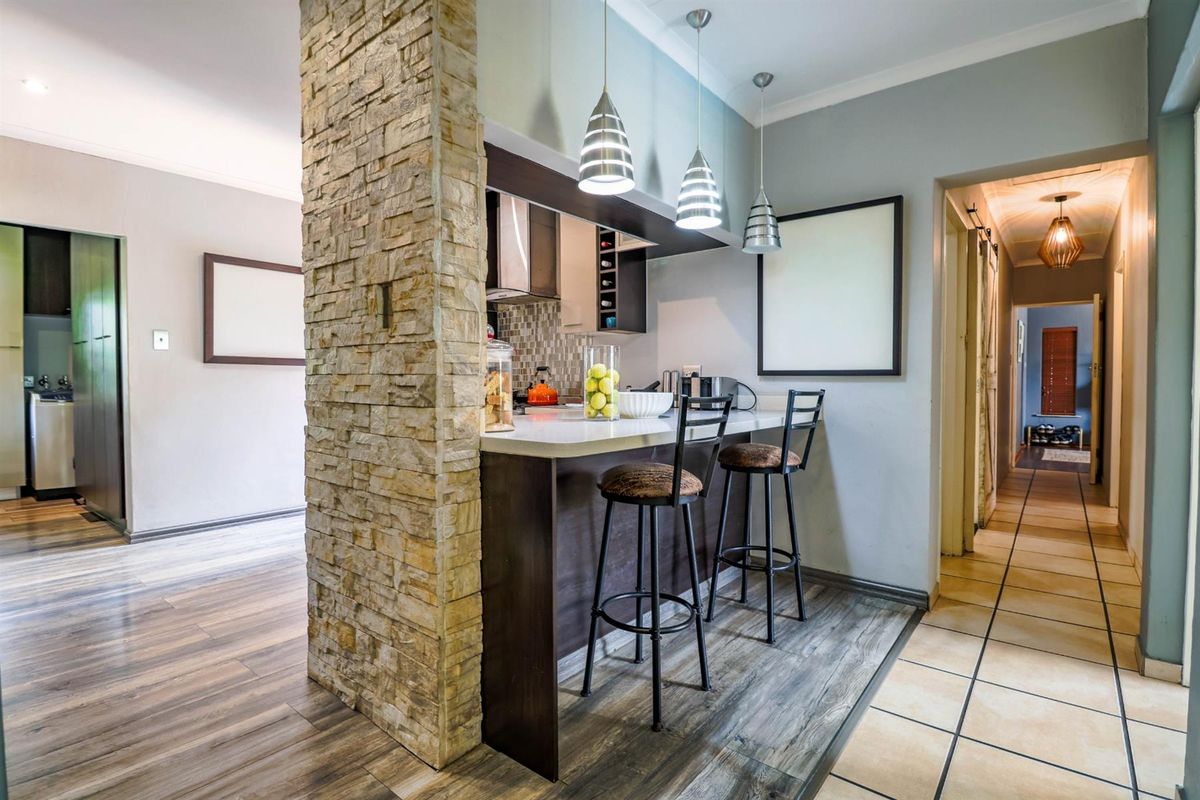A modern kitchen featuring a stone-clad breakfast bar, sleek cabinetry, and pendant lighting, seamlessly connecting to the adjacent living and hallway areas.