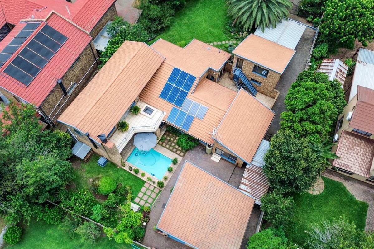 Aerial view of the property showcasing the tiled roof, solar panel installation, swimming pool, and landscaped garden area.