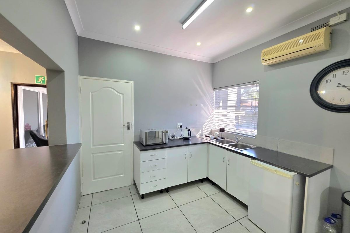 Compact kitchen area featuring white cabinetry, dark laminate countertops, stainless steel sink, tiled flooring, and a wall-mounted air conditioning unit.