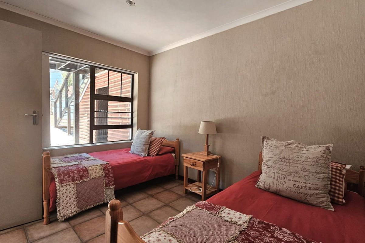 A functional bedroom featuring tiled flooring, a large window providing natural light, and neutral wall finishes.