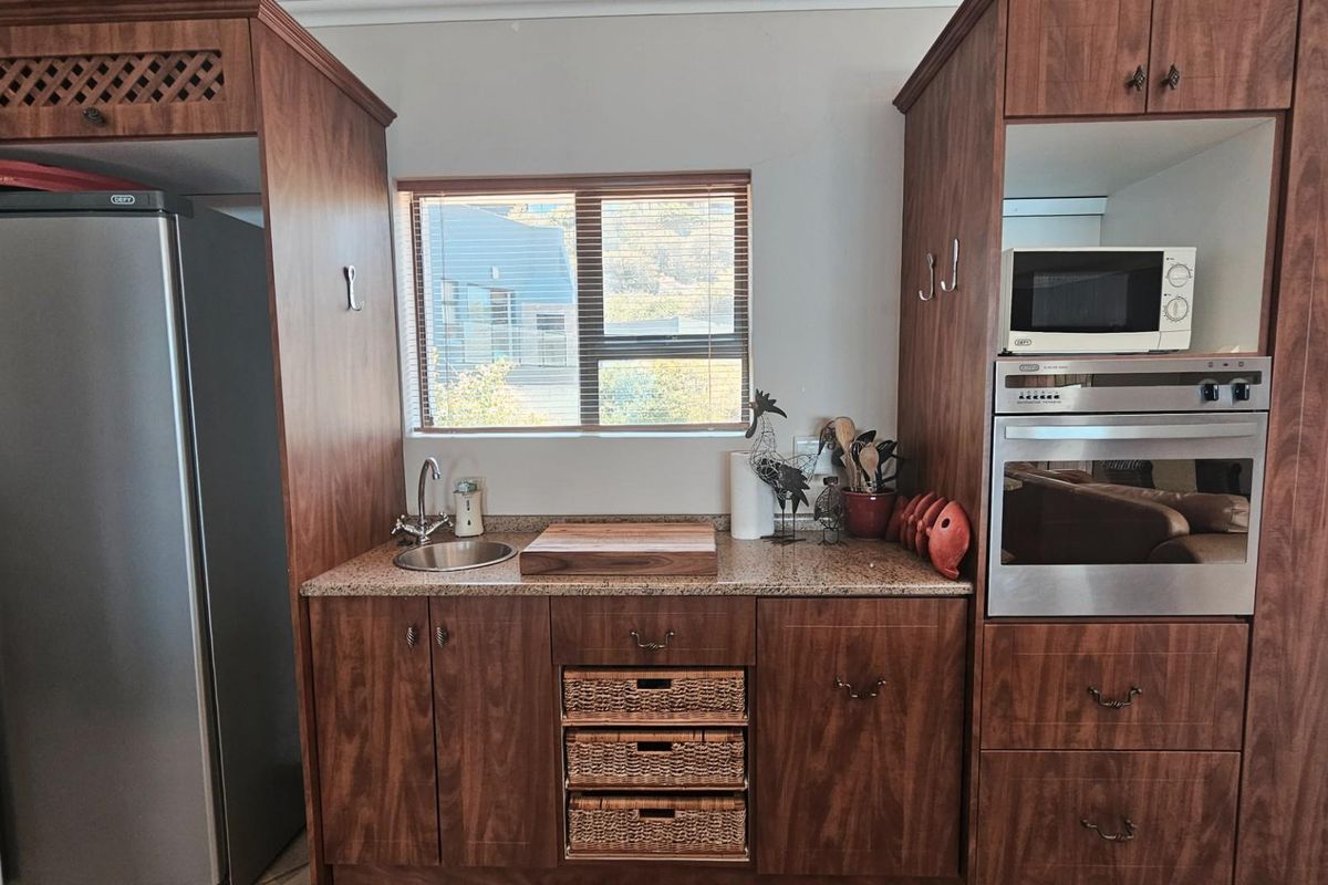 A compact kitchen area featuring wood-finish cabinetry, granite countertops, a built-in oven, and a stainless steel sink.